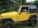 2001 Jeep Wrangler - A mud-covered yellow Jeep Wrangler is parked outdoors with a driver inside.