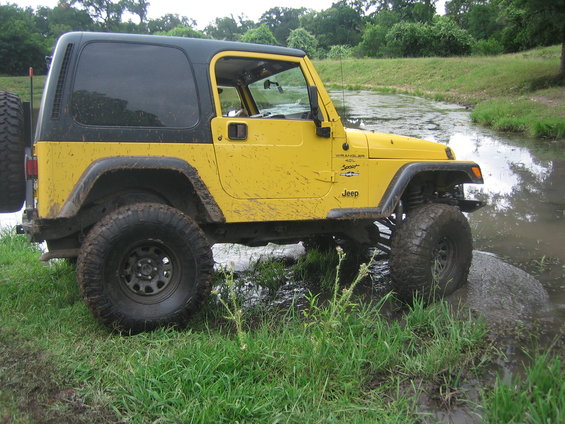 Yellow Jeep Wrangler with black hardtop, mud splatters, and off-road tires, partially submerged in water