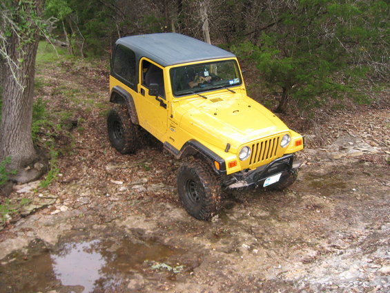 Yellow Jeep Wrangler on a dirt path with trees and rocks