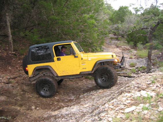 Yellow 2001 Jeep Wrangler with a hardtop driving on a rocky, wooded trail