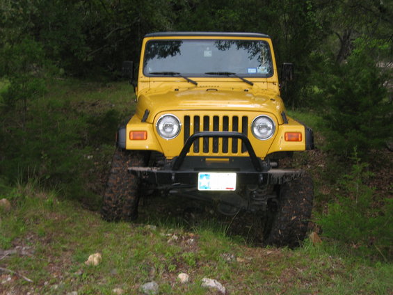 Yellow Jeep Wrangler parked on grassy slope with trees in background