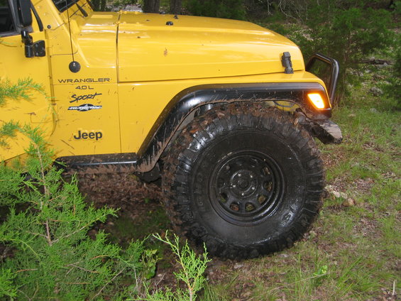 Yellow 2001 Jeep Wrangler 4.0L Sport with mud on tires and fender flares, parked off-road