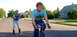 1986 Ford Bronco - One person rides a bicycle while towing another person on roller skates down a residential street.