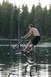 1986 Ford Bronco - A man rides a bicycle on one wheel across a body of water, with a forest behind him.