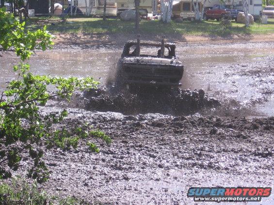 Off-road truck driving through deep mud, kicking up spray