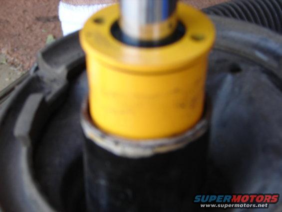 Close-up of a yellow suspension strut mount on a black shock absorber