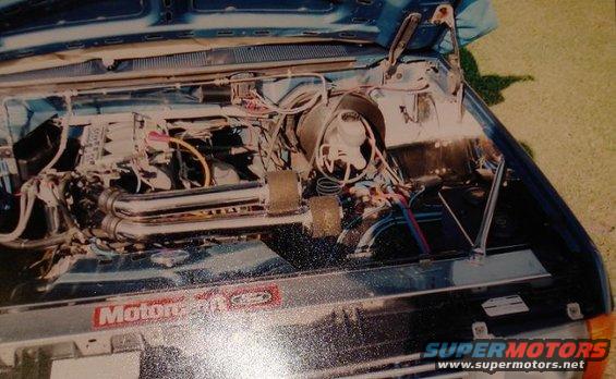 Engine bay with chrome exhaust headers and various hoses and wires. "Motor" logo visible