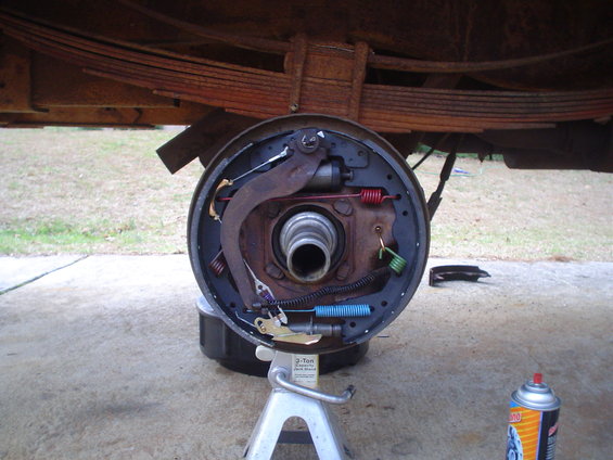 Vehicle brake drum assembly disassembled on jack stand. Leaf springs visible above