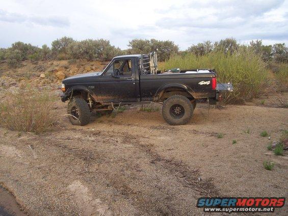 Black 1994 Ford F-150 pickup truck parked on dirt road with brush and hills in background