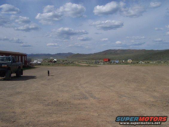 1994 Ford F-150 parked in dirt lot, dog nearby, other vehicles and buildings in background