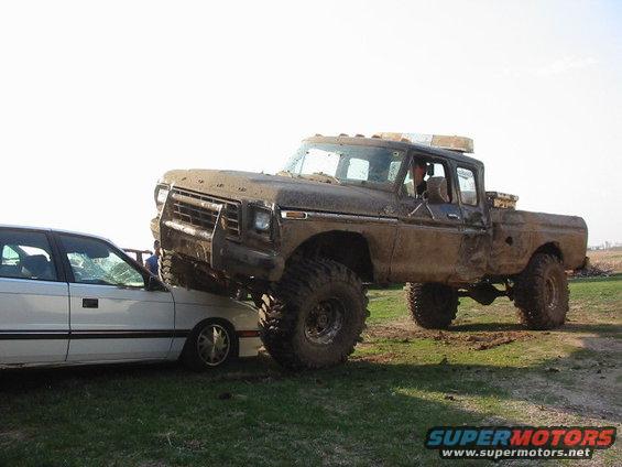 Muddy 1979 Ford F-250 lifted high, crushing a white sedan