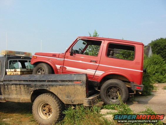 Red Suzuki Samurai loaded into a flatbed truck, side view