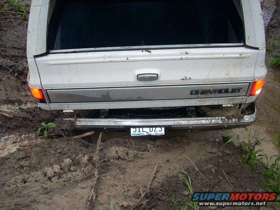 Rear view of a white Chevrolet pickup stuck in mud, license plate visible
