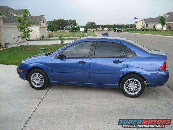 Blue sedan parked on a concrete driveway, side view. Visible wheels and doors