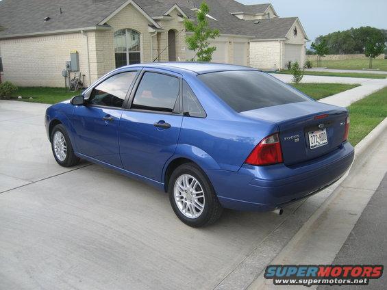 Blue sedan parked on a concrete driveway, rear quarter view. The car has tinted windows and a license plate reading 272-HDD