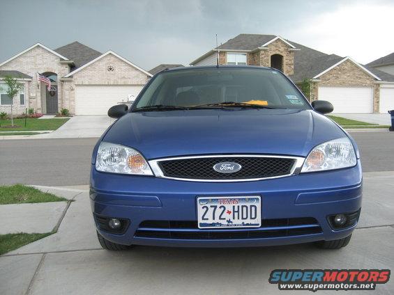 Blue Ford Focus parked in driveway, front view. Houses and cloudy sky in background