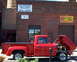 1971 Porsche 914 - A red pickup truck is parked outside a brick building with multiple signs, its hood open to reveal the engine.