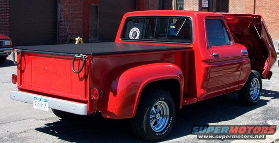 Red pickup truck with a black tonneau cover and chrome wheels, rear 3/4 view