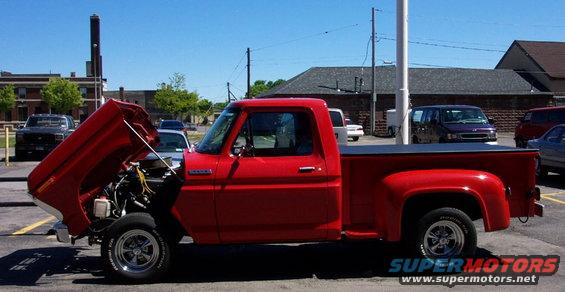 Red pickup truck with hood open, showing engine. Other vehicles and buildings in background