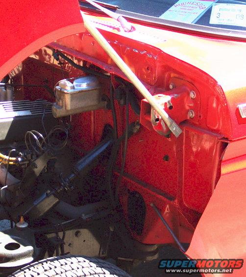 Close-up of a red car's engine bay, showing the brake fluid reservoir and various hoses