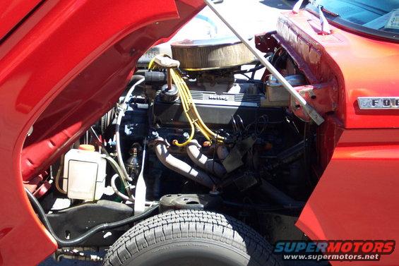 Red truck engine bay with V8 engine, air cleaner, and yellow spark plug wires. "FORD" emblem visible on fender
