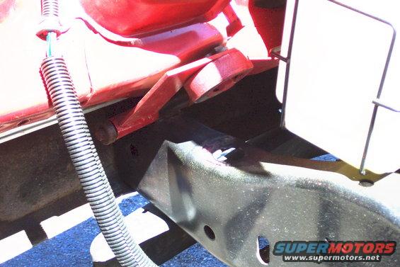 Red metal bracket attached to a black chassis with a ribbed black hose nearby