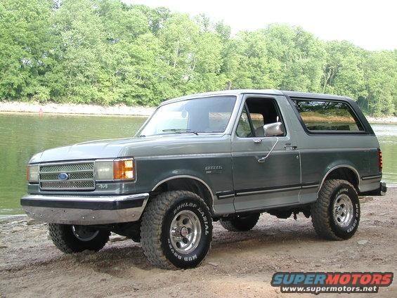 1989 Ford Bronco parked by a body of water with trees in the background