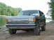 1989 Ford Bronco - This Ford Bronco is parked on a dirt bank next to a body of water, with trees in the background.
