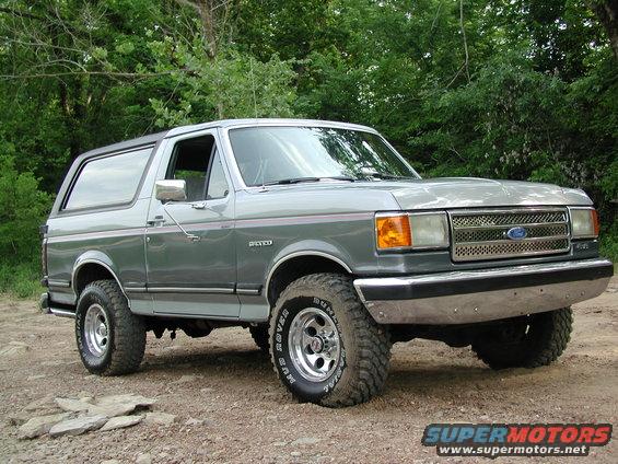 Silver Ford Bronco with aftermarket wheels and tires, parked on a dirt road