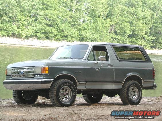 Two-tone gray Ford Bronco with aftermarket wheels and tires parked on dirt near water
