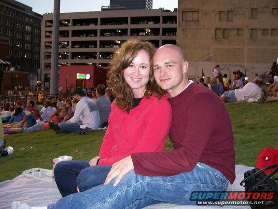 Couple on grass at outdoor event, buildings in background