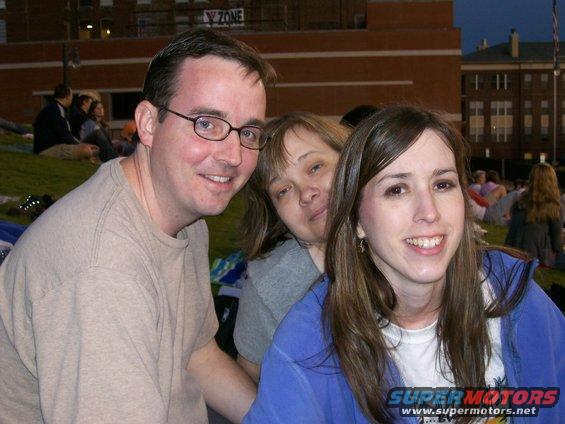 Three people smiling at an outdoor event with buildings in the background