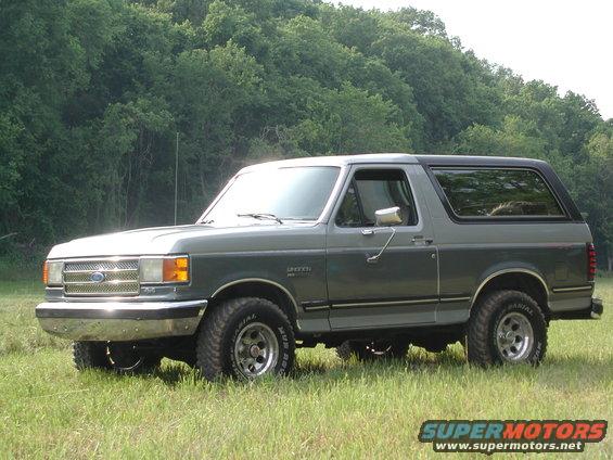 Gray two-tone Ford Bronco parked in grassy field, front quarter view