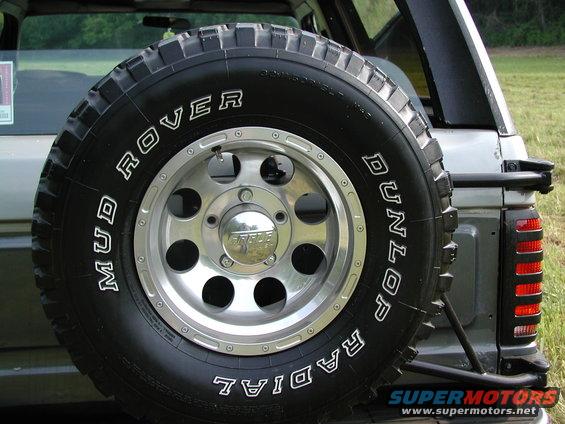 Spare tire mounted on the rear of a silver SUV, showing a Dunlop Mud Rover radial tire on a chrome rim