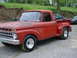 1965 Ford F-100 - A red 1965 Ford F-100 pickup truck is seen from a three-quarter front angle, with other vehicles in the background.