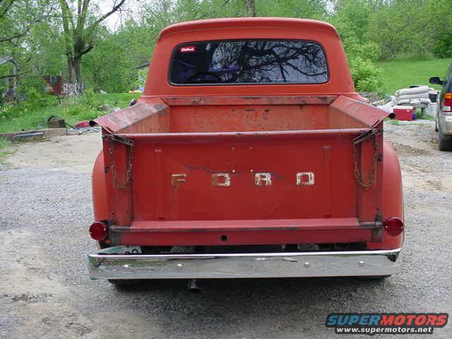 Rear view of a red Ford pickup truck. The tailgate has 'FORD' spelled out in block letters. Chrome bumper and round taillights are visible