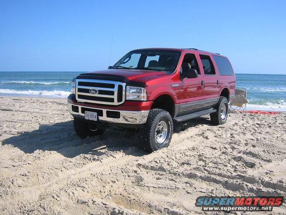 Red 2005 Ford Excursion parked on a beach with ocean in background