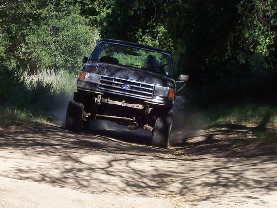 Black Ford F-Series truck with lifted suspension driving on a dirt road, kicking up dust