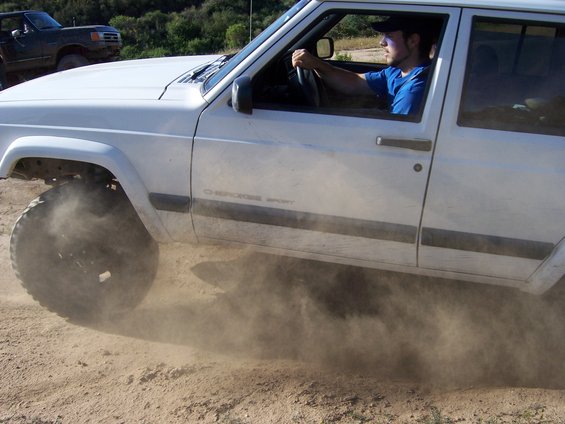 White Jeep Cherokee Sport kicking up dust on a dirt road, driver visible
