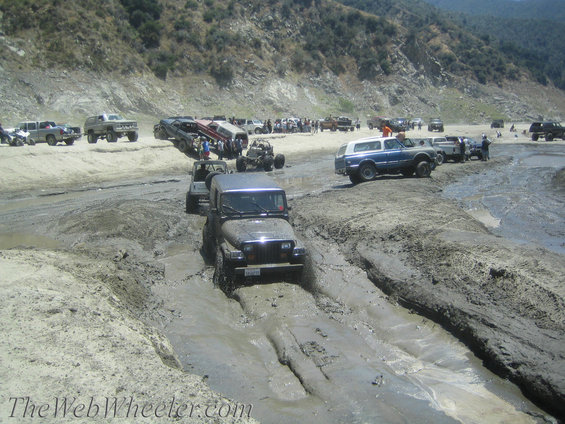 Dark gray Jeep Wrangler driving through mud, front view. Water and mud splash