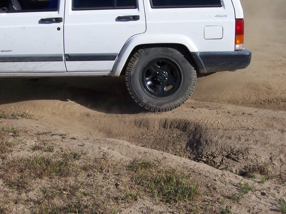 White Jeep Cherokee XJ side view, rear wheel kicking up dirt on a trail