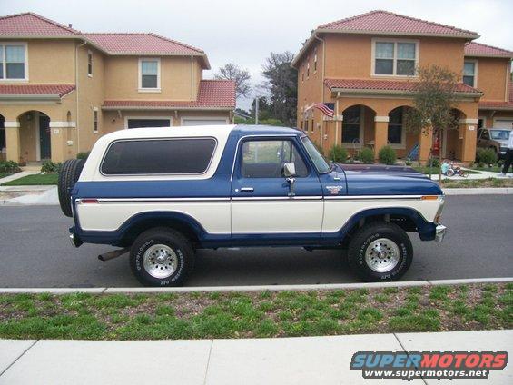 1979 Ford Bronco parked on street, side view. Blue and white two-tone paint, white hardtop, spare tire on rear