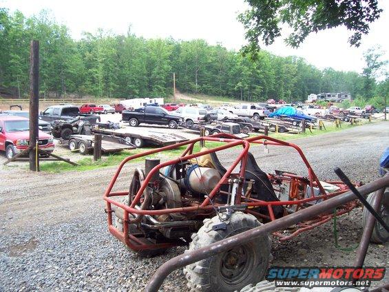 Red dune buggy with exposed engine and large tires parked in a lot with other vehicles and trailers