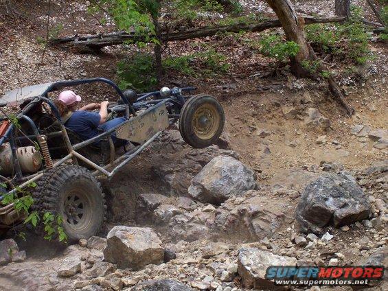 Buggy with a pink hat driver going over rocks on a trail