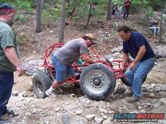 Red off-road buggy with men pushing it on rocky terrain