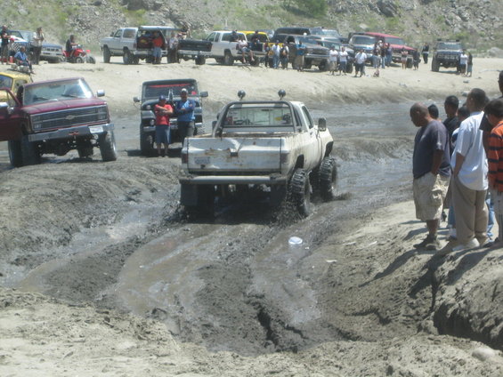 White pickup truck with large tires driving through mud, rear view