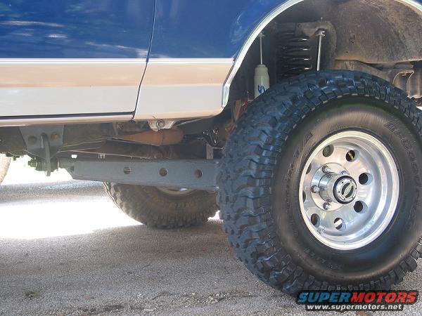 Close-up of a blue and tan Ford Bronco's front wheel and suspension, showing a lift kit
