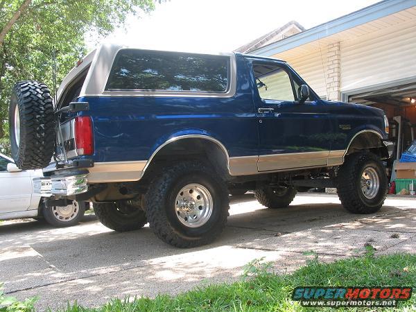 Blue 1996 Ford Bronco with a lifted suspension and a spare tire on the rear, viewed from the rear-right