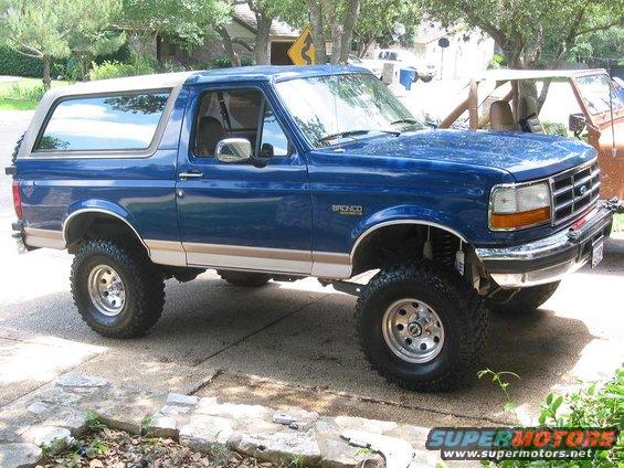 Blue Ford Bronco with tan stripe, lifted suspension, and aftermarket wheels parked on a driveway