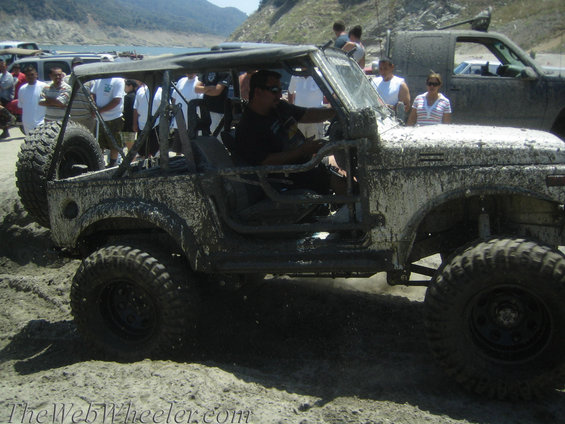 Mud-covered 1987 Suzuki Samurai with a soft top, off-roading in sand and water